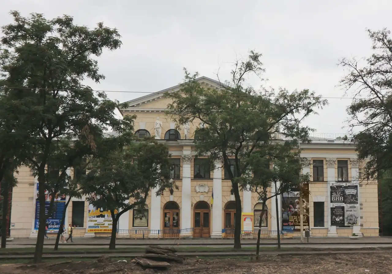 Фасад ДРАМіКОМу, колишнього Зимового театру, за деревами проспекту Яворницького