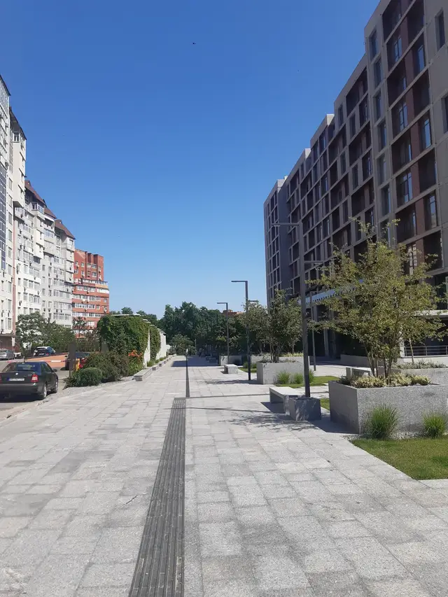 Сонячна пішохідна вісь Бульвару Кучеревського з лавами, молодими деревами й небагатьма перехожими
