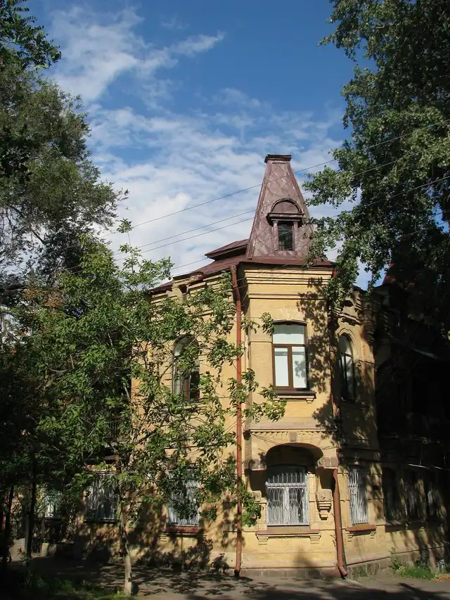 Жовтоцегляний фасад житлового будинку на Мусліма Магомаєва, 19 серед зелених дерев без людей