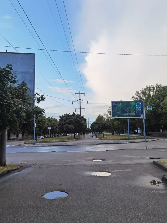 Зелена бульварна алея проспекту Олександра Поля після дощу з кількома перехожими вдалині