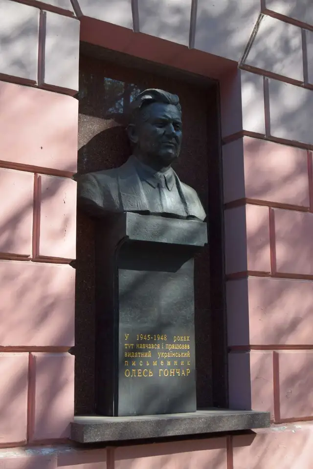 Бронзове погруддя Олеся Гончара з меморіальним написом на фасаді будинку у Дніпрі
