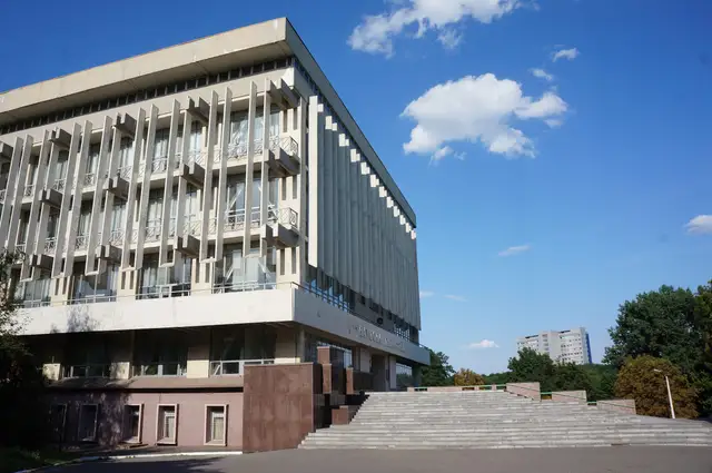 Модерністська будівля наукової бібліотеки університету з вертикальними ребрами фасаду, широкими сходами та висотним головним корпусом позаду