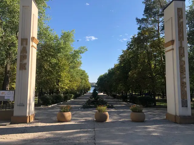Центральний вхід до Придніпровського парку з двома пілонами, алеєю між деревами й Дніпром у перспективі