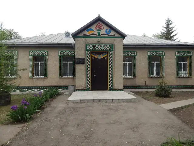 Одноповерхова будівля історико-краєзнавчого музею села Спаське з орнаментованими лиштвами, меморіальною дошкою біля входу та квітником